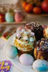 Obraz premium Festive Easter celebration with traditional cakes (Kulich) topped with chocolate, nuts, and marshmallows, surrounded by pastel-colored eggs. Ideal for holiday marketing and blogs.