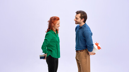 Man and woman hiding gifts behind backs before exchange. Concept of Saint Valentines Day, surprise...