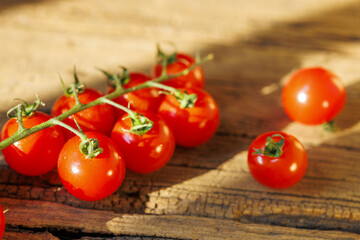 Bright red cherry tomatoes on rustic wooden surface, basking in warm sunlight, create fresh and vibrant scene. tomatoes glossy skin and green stems add touch of natural beauty