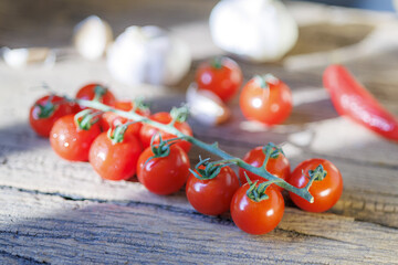 Fresh cherry tomatoes on vine rest on rustic wooden surface, surrounded by garlic and red chili pepper, creating vibrant and inviting culinary scene