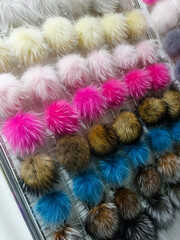 Display of colorful fur pom poms in a craft store showing various colors and sizes hanging in rows under bright lights