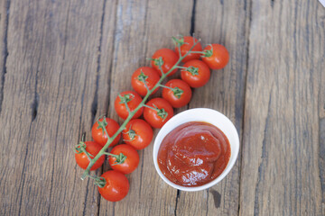 Fresh cherry tomatoes on vine next to bowl of rich tomato sauce on rustic wooden table. vibrant red color of tomatoes contrasts with natural wood texture, creating fresh and appetizing scene