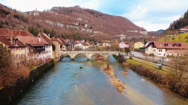 Aerial view of the town showcasing the bridge over the river, with houses nestled against the backdrop of the hills, Clos du Doubs, Jura, Switzerland.