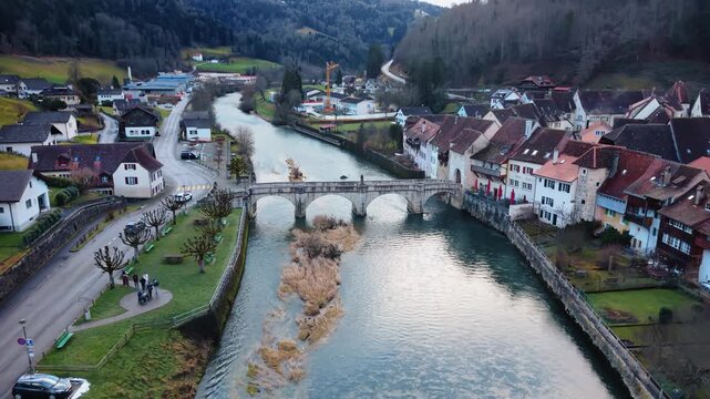 Aerial view of the stone bridge over the Doubs river with buildings and trees, creating a picturesque scene, Clos du Doubs, Jura, Switzerland.
