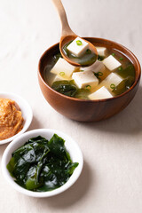 Healthy Japanese miso soup with soft tofu and seaweed in a wooden bowl being scooped with a spoon