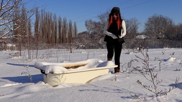 A beautiful girl with a diary in her hands near an old bathtub in the middle of a snowy landscape plans her day. A combination of fashion, nature and an old bathtub.