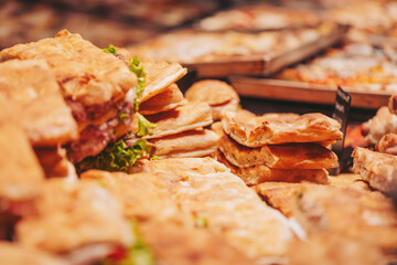 Bakers display a variety of fresh bread and pastries on wooden trays at a food market. Customers browse the selection in the warm afternoon light, enjoying the aroma and flavors