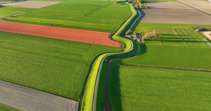 Aerial view of a winding road on a dam surrounded by fresh green fields. Drone shot of an asphalt path curving through the rural countryside on a bright sunny day. Scenic transportation infrastructure