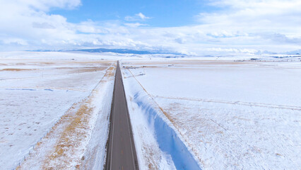 Obraz premium DRONE: Flying along a long straight road leading through the wintry Montana
