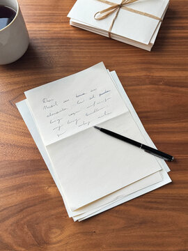 Vintage style stationery flat lay with handwritten letter and tea. Top view of a handwritten letter, reading glasses, and a stack of craft envelopes tied with string on a warm wooden background