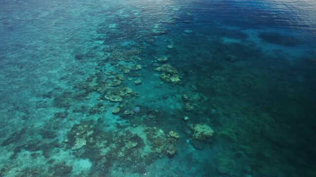 Drone push-in aerial shot flying over shallow coral reef toward Frankland Island, surrounded by clear turquoise water in the Great Barrier Reef