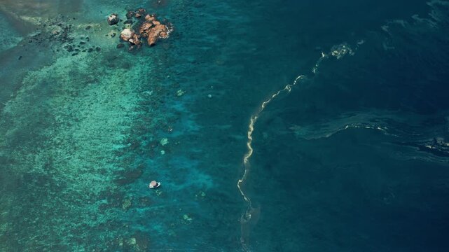 Wide aerial drone shot showing coral reef transitioning into deeper blue ocean near Frankland Islands, Great Barrier Reef.