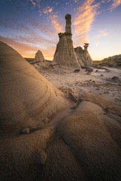 View of majestic, layered rock formations rise from the arid landscape under a vibrant sunset sky painting the scene with gold and blue hues, Farmington, New Mexico, United States.