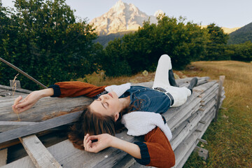 Obraz premium Woman relaxation on wooden platform in countryside meadow with mountain and nature views, lying outdoors in denim jacket and shearling, peaceful summer rest and scenic escape.