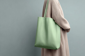 Green bag hangs from a shoulder against a gray wall