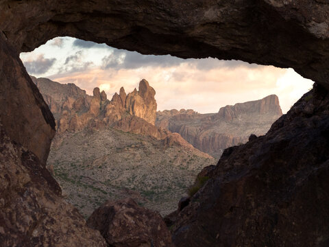 View of jagged peaks pierce the sky through a natural rock window, framing the rugged beauty of the desert landscape, Nipton, California, United States.