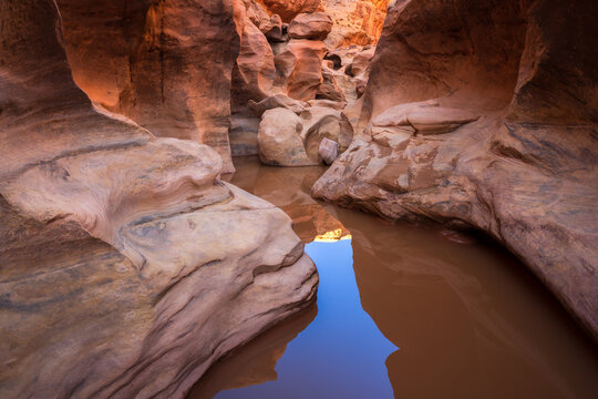 View of reflections dance on the still water snaking through the sculpted sandstone canyon walls, a mix of shadow and light in Escalante, Utah, United States.