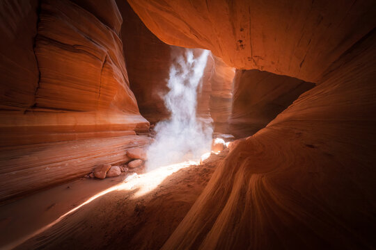 View of light streams through the textured, orange-red sandstone slot canyon, illuminating the swirling dust motes in Escalante, Utah, United States.