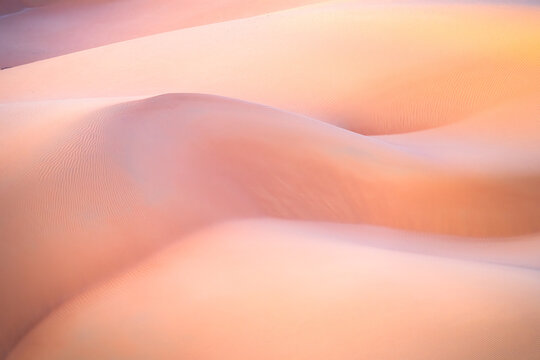 View of soft, rolling sand dunes bathed in the warm glow of sunset, creating a serene and ethereal landscape, Ubar, Dhofar Governorate, Oman.