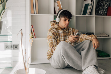 young man with headphones and mobile phone sitting on the floor indoors