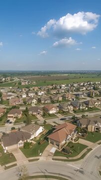 Vertical video: Ascending drone pulling back over suburban cul de sac, revealing homes and farmland