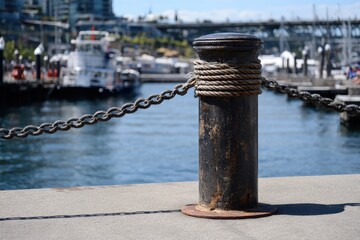Fototapeta premium Metal post with rope on pavement and boat behind