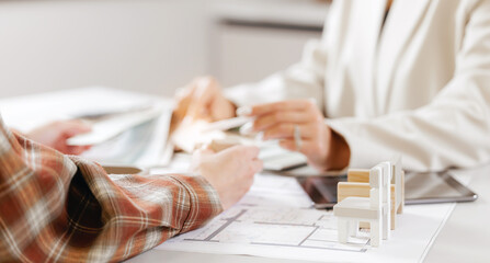 Collaborative business meeting with focus on architectural plans and model on table, presentation of design interior