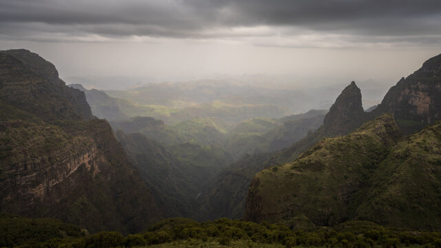 View of imposing, verdant mountains under a moody sky, creating a dramatic landscape of light and shadow in a remote, wild setting, Amhara, Ethiopia.