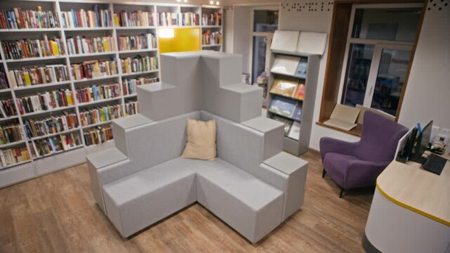 No people full shot of public library interior with bookshelves, computer desk and comfortable couch with modern unusual design for visitors