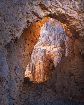 View of a sunlit cavernous opening with rough rock textures and hues of orange and blue, creating a dramatic contrast, Djanet, Illizi Province, Algeria.