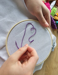 Hands work with purple thread in an embroidery hoop on a white fabric background during a craft session © Nadzeya