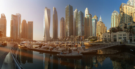 Fototapeta premium Evening view of the city. Orange sunlight, skyscrapers, buildings, and city streets. On the streets of the Emirates, in a public space.