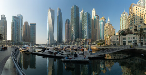 Obraz premium Evening view of a river canal and a ship. Orange sunlight, skyscrapers, buildings and the embankment. On the streets of the Emirates, in a public place.