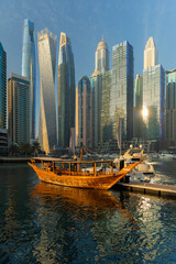 Evening view of a river canal and a ship. Orange sunlight, skyscrapers, buildings and the embankment. On the streets of the Emirates, in a public place.