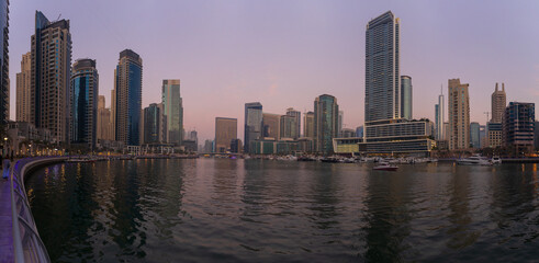 Fototapeta premium Evening view of the city. Orange sunlight, skyscrapers, buildings, and city streets. On the streets of the Emirates, in a public space.