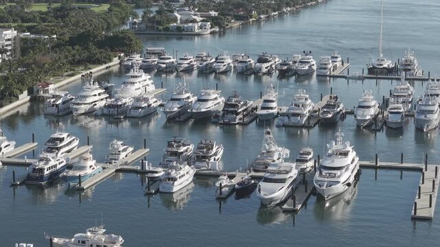 Aerial view of many yachts docked in a harbor, reflecting sunlight on the tranquil water, a scene of wealth and leisure, West Palm Beach, Florida, United States.