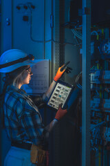 Female electrician manages switchgear inspection with tablet in tech room. Panel automation.