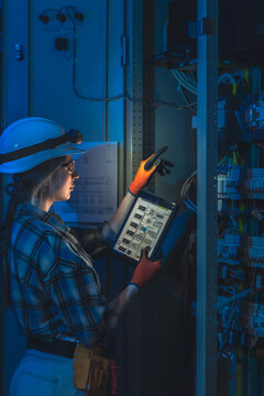 Female electrician manages switchgear inspection with tablet in tech room. Panel automation.