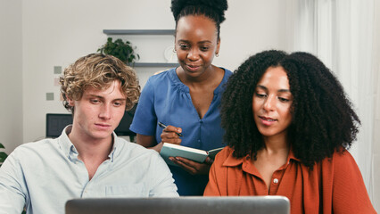 Diverse Trio Collaborating on Laptop in a Modern Startup Office Setting for Teamwork and Innovation