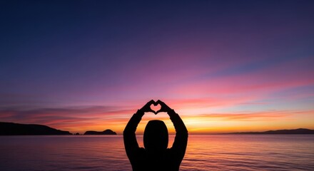 Silhouette of hands forming a heart against a vibrant sunset sky over tranquil water good night love
