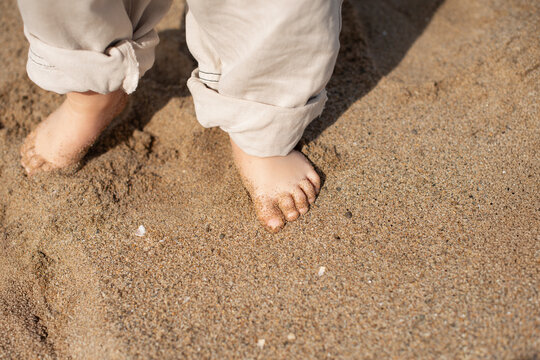 Close-up of baby feet standing barefoot on warm beach sand. Natural light, soft textures, and minimal composition convey childhood, innocence, summer, and first steps. Ideal for concepts of family, gr
