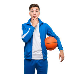 Young Man in Blue Tracksuit Holds Basketball, Hand on Chin &mdash; Thoughtful, Playful, Athletic &mdash; Ideal for Youth Sports, Basketball Culture, or Fitness Strategy Branding.