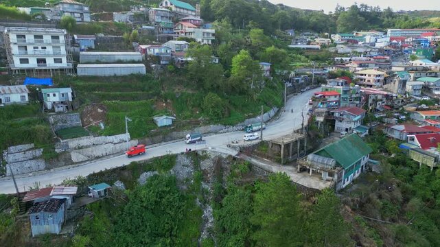 Downward side view aerial of a hillside road in Atok, Benguet, following the highway as it cuts through steep terrain and dense mountain housing.