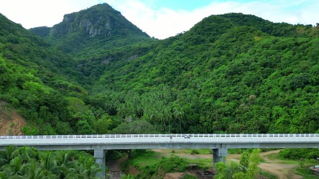 Rising wide aerial reveals the long white bridge of Lobo, Batangas, spanning a lush valley between dense tropical forests and jagged mountain peaks.