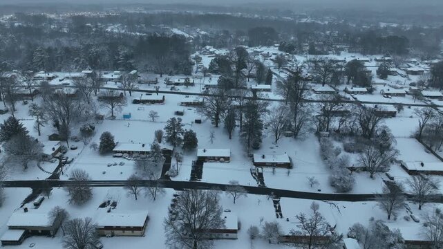 Row of snowy houses and homes on cold cloudy winter day. Aerial flyover wide shot. Leafless trees in suburb neighborhood. Foggy morning in USA.