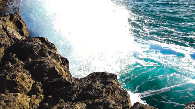 Slow motion downward view from Boca do Inferno as powerful turquoise Atlantic waves slam into eroded jagged cliffs, exploding into bright white foam under sunny coastal light in Cascais seaside