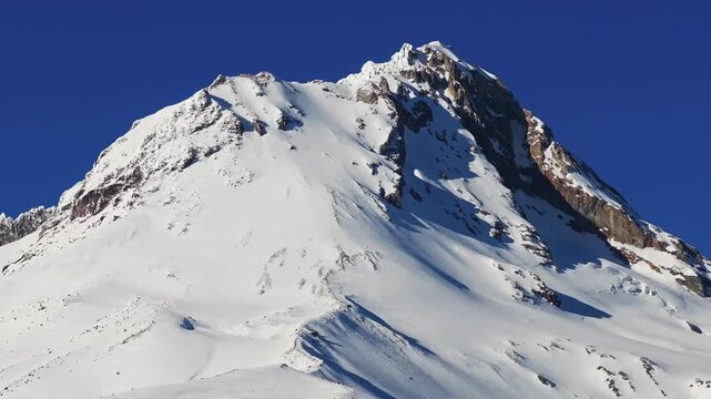A medium panning drone view of Mount Hood and its steaming fumarole crater with glaciers and heavy snowpack at the summit of the lone volcano in the Pacific Northwest near Hood River and Portland OR