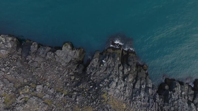 Fisherman's on basaltic rocks, waves splashing into volcanic cliff - aerial 4k