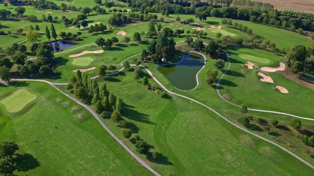High aerial overview of expansive golf course with ponds fairways and surrounding greenery, drone medium backdrop dolly
