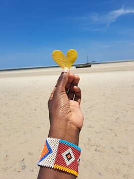 An African woman holding a heart-shaped yellow leaf  on the beach